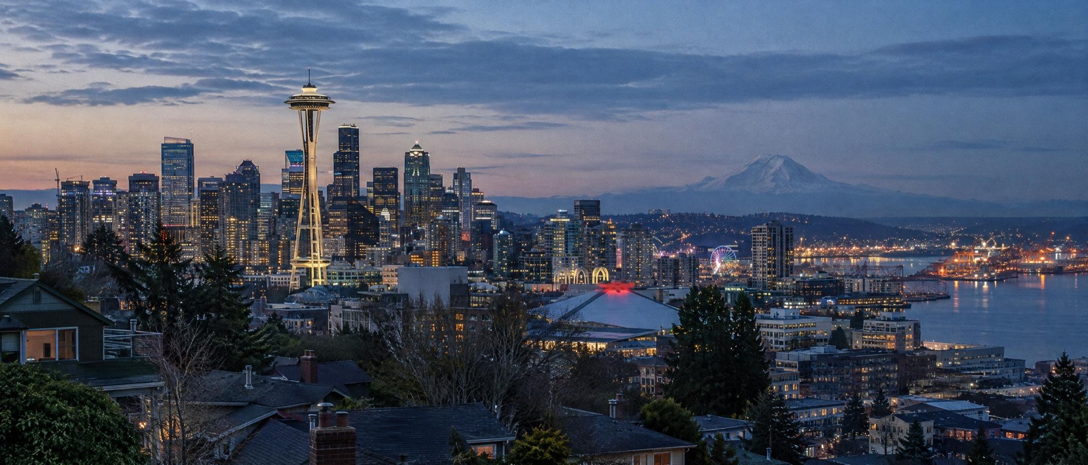 Downtown Seattle and the Space Needle at blue hour, seen from the Queen Anne side over rooftops and evergreens, with Mount Rainier on the horizon and Elliott Bay lit up at right